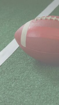 Vertical video: Camera pulling back revealing still football on turf showing laces and field line