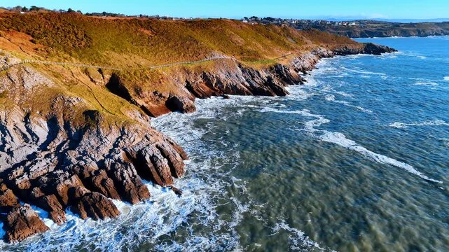 Close up aerial view of jagged cliff rocks Wales. High angle shot of geological rock formations and coastal path with crashing waves in Wales UK
