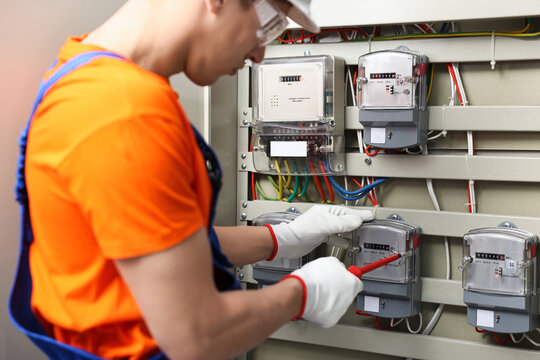 Electrician with screwdriver checking electrical meter indoors, closeup