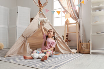 Little girl playing with toys near toy wigwam in playroom, space for text © New Africa
