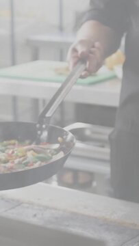 Vertical video: Chef flipping vegetables for service in busy kitchen, pan tilting, tongs guiding