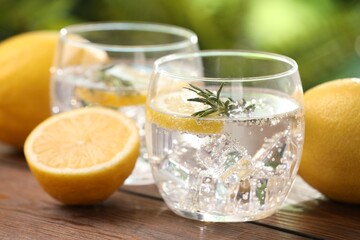 Obraz premium Sparkling water with lemon and rosemary on wooden table against blurred background, closeup