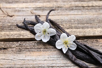 Fototapeta premium Vanilla pods and flowers on wooden table, closeup