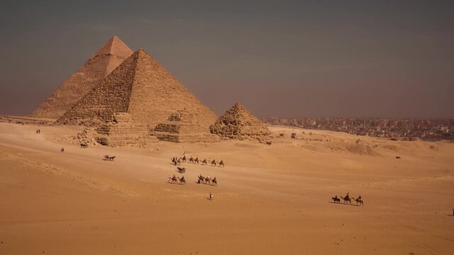 Tourists walking and riding camels in desert valley with Giza pyramids. A cinematic view of desert valley near Giza plateau, with tourists exploring on foot, riding camels, and in horse-drawn carriage