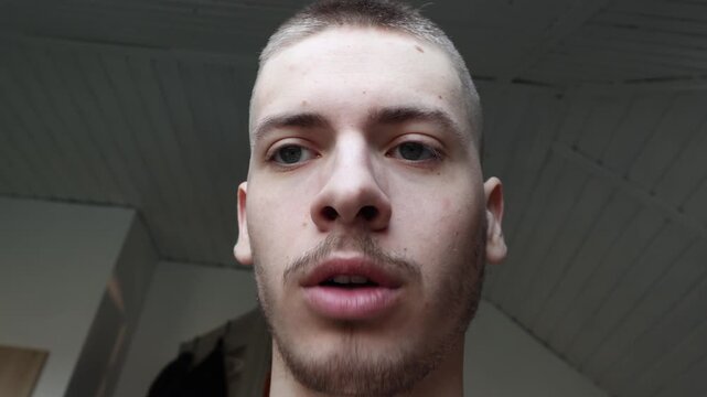 Low angle portrait of young Gen Z man looking down at camera, talking on video call or reacting to smartphone content, casual vlog