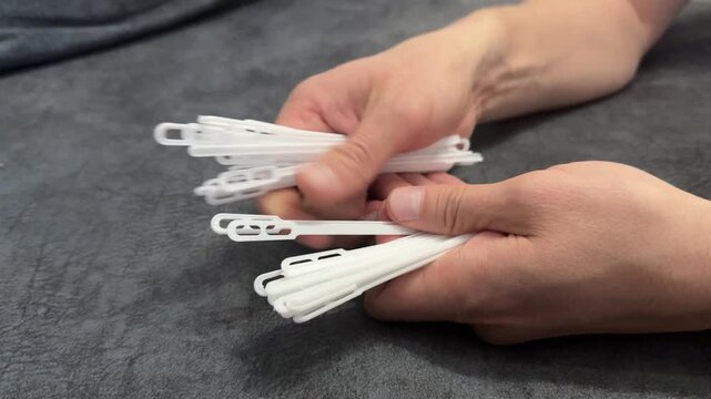 Hands holding multiple white plastic clothing tags. Packaging or retail concept, detail on everyday materials used for labeling and merchandise