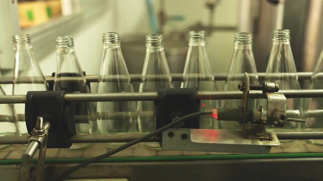 Close-up of industrial bottling equipment precisely filling glass containers with liquid during high-speed beverage production process in factory