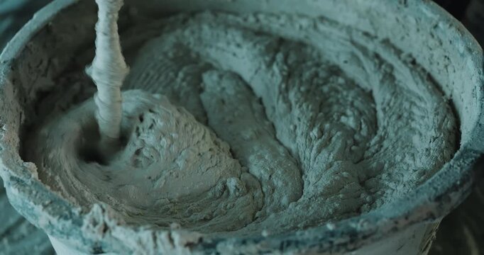 Blending cement mortar in bucket with power mixer creating circular motion close up