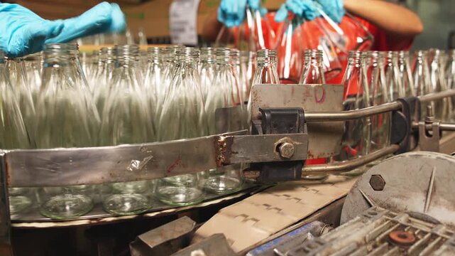 Close-up of industrial bottling equipment precisely filling glass containers with liquid during high-speed beverage production process in factory