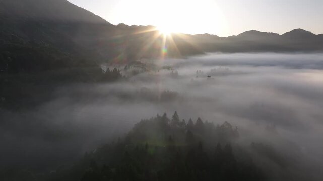 Morning sunlight pierces through misty cloud sea over mountain ridges terraced fields and rural villages