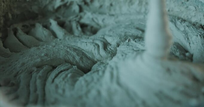 Mixing cement mortar in bucket with electric mixer forming thick texture close up