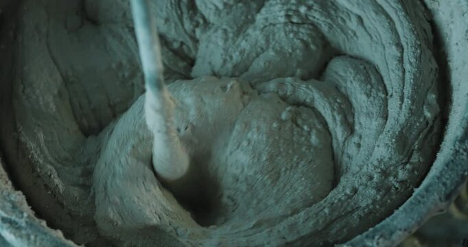 Mixing cement mortar in bucket with electric mixer creating swirl close up