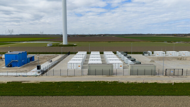 Dronten, Netherlands - 04 April 2026: Aerial view of the Olsterdwarspad battery energy storage system with rows of white container units and a wind turbine base near agricultural fields.