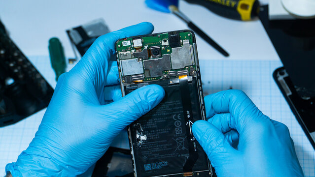  Close up of technician repairing smartphone motherboard with tools. Mobile phone service, electronics repair and hardware maintenance concept.
