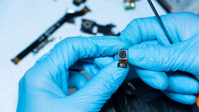 Macro shot of smartphone camera module held by technician. Mobile repair, spare parts and electronics service concept.