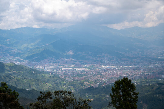 A stunning panoramic view of the Medell&iacute;n and Envigado skyline in Colombia, captured from a high Andean mountain peak. The photograph showcases the dense urban valley filled with iconic red-brick high