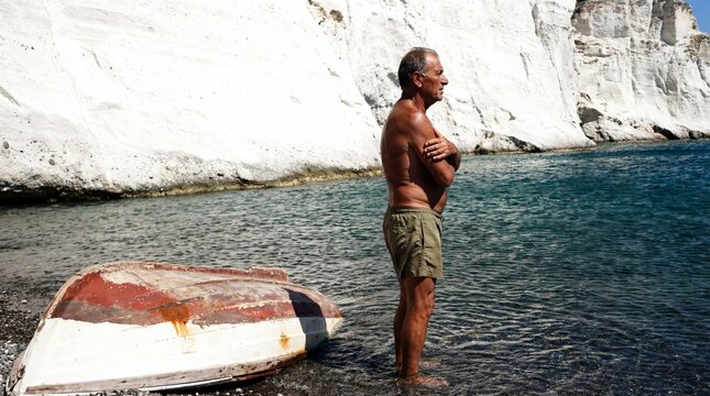 Senior Man Wading in Clear Water by White Sea Cliffs with Small Boat