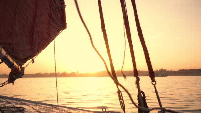 Atmospheric close-up of felucca boat at sunset in Luxor. Close-up shot of a traditional felucca boat on the Nile River at sunset. The camera captures parts of the boat, ropes, and sail