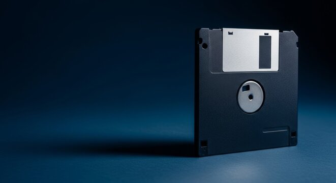 Retro floppy disk with metallic label casting sharp shadow on dark navy blue background, symbolizing data storage and digital technology concepts.