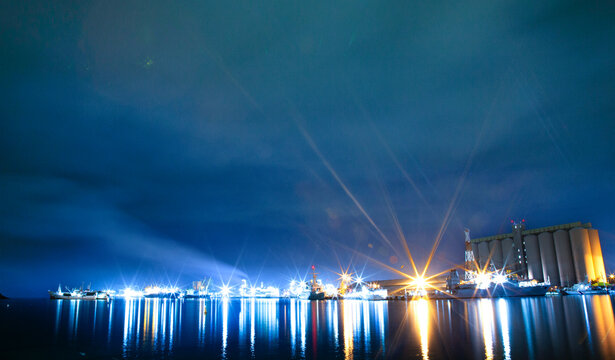 Port Louis harbour illuminated at night, Caudan Waterfront, Mauritius. Long-exposure shot capturing dramatic starburst lights and reflections on the calm water with grain silos and docked vessels.