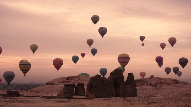 Hot air balloons at sunrise over ruins near Hatshepsut Temple, Luxor. Sunrise scene near Hatshepsut Temple in Luxor, Egypt, showing numerous hot air balloons rising in the early morning sky.