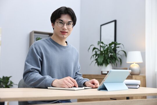Young student studying with tablet at wooden table indoors