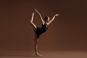 Obraz premium Graceful ballerina in black dress practicing dance moves on brown background