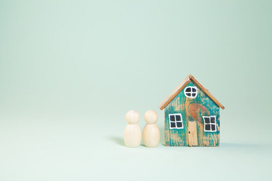 Miniature people with wooden house on pastel color background, family concept