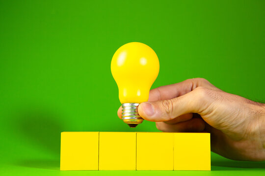 Yellow lightbulb on wooden cubes with human hand on green background