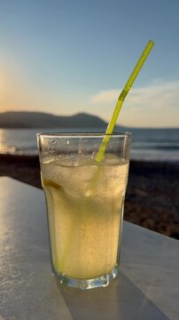 Glass of fresh lemonade with straw near sea view in summer setting, ideal for lifestyle and hospitality marketing. Citrus beverage highlights refreshment, relaxation and travel experience