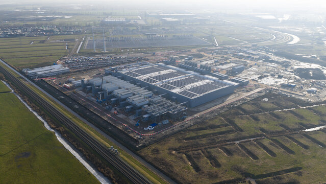 Groningen, Netherlands - 20 January 2026: Aerial view of Datacenter Westpoort featuring its large industrial structure and cooling systems surrounded by green fields and a railway line.