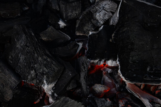 Close up of smoldering charcoal with glowing embers and ash texture in low light, ideal for fire, heat, grilling, fuel, and dramatic background concepts.