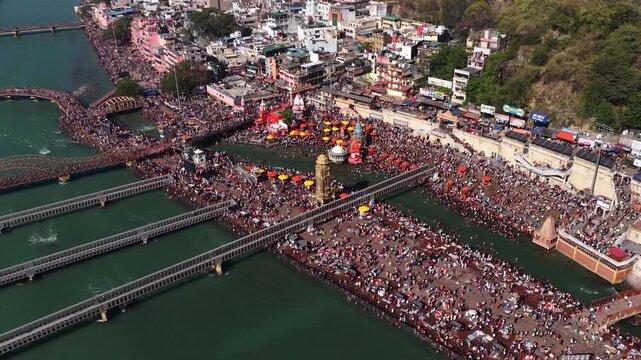 A pull back aerial drone shot of Har Ki Pauri in Haridwar, showing massive crowds gathered along the banks of the Ganges River.
