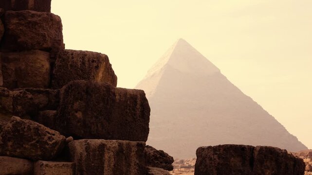Camera reveal of Great Pyramid stone blocks foreground with central pyramid silhouette in hazy morning Giza Egypt. A smooth camera movement reveals textured stone blocks of the Great Pyramid