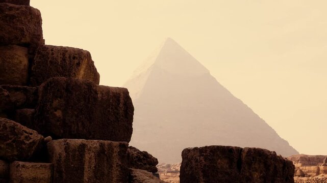Smooth backward reveal of Great Pyramid from foreground stone blocks to full structure with central pyramid in hazy morning Giza Egypt. A smooth backward camera movement