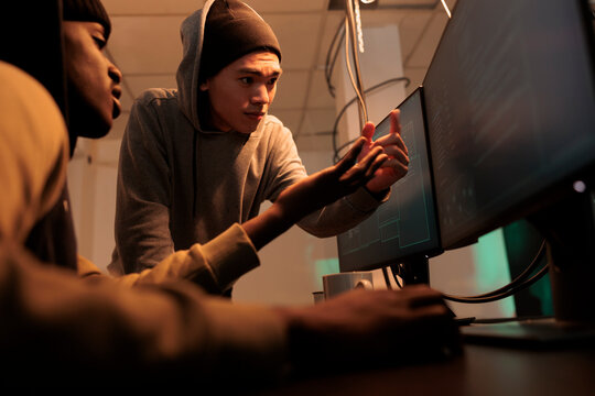Internet criminals discussing computer system hacking, cyberattack. Hackers in hoodies coding password cracking pogram, scammers programming malicious software at night time