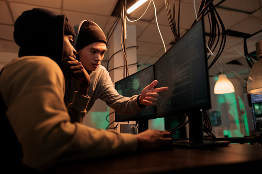 Hackers discussing computer system hacking, coding malicious software, cybercrime. Criminals planning cyberattack, programming internet virus, stealing data at night time