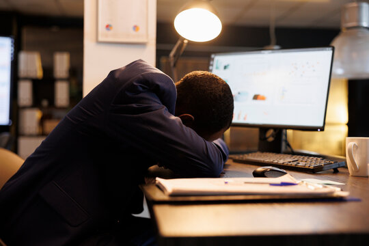 Workaholic businessman slepping desk in startup office, after checking marketing statistics on computer. Exhausted tired entrepreneur working overtime at company strategy plan. Business concept