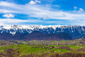 Fototapeta premium The snowy ridges of the Piatra Craiului Mountains seen from the green hills of the village of Măgura in Romania