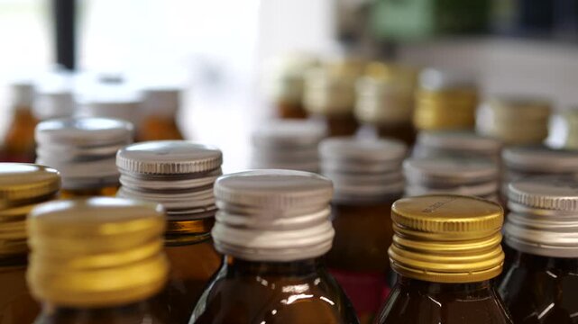 Close up view of numerous brown glass medical bottles arranged in neat rows, featuring both gold and silver screw caps with a shallow depth of field creating a soft, blurred background