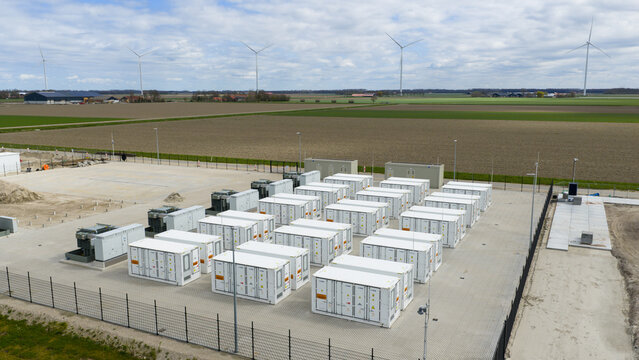 Dronten, Netherlands - 04 April 2026: Aerial view of the Olsterdwarspad battery storage facility with white containers and wind turbines under a cloudy sky in Dronten, Flevoland, Netherlands.