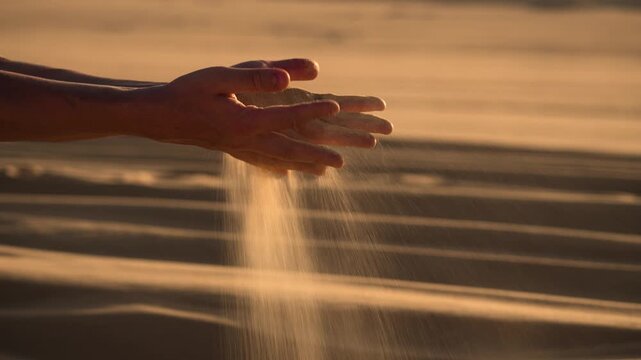 Hands letting sand fall in Egyptian desert. Close-up of hands holding sand, letting it slowly fall as the golden grains cascade down. The vast desert stretches out softly blurred in the background