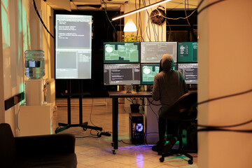 Young hacker working on multiple monitors to hack online server, cracking firewall encryption to steal passwords. Professional thief looking at screen planting trojan virus at night. © DC Studio