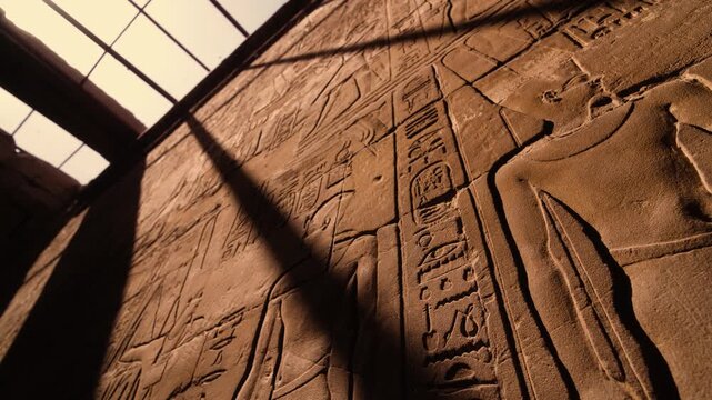 Sunlit wall with hieroglyphs in Luxor Temple. Smooth cinematic shot looking upward inside a chamber of Luxor Temple, capturing a decorated wall with ancient Egyptian hieroglyphs and figures.