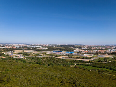 Alcabideche, Portugal - 03 April 2026: Aerial view of the Autodromo Fernanda Pires da Silva racing circuit surrounded by green hills and urban landscape under a clear blue sky.