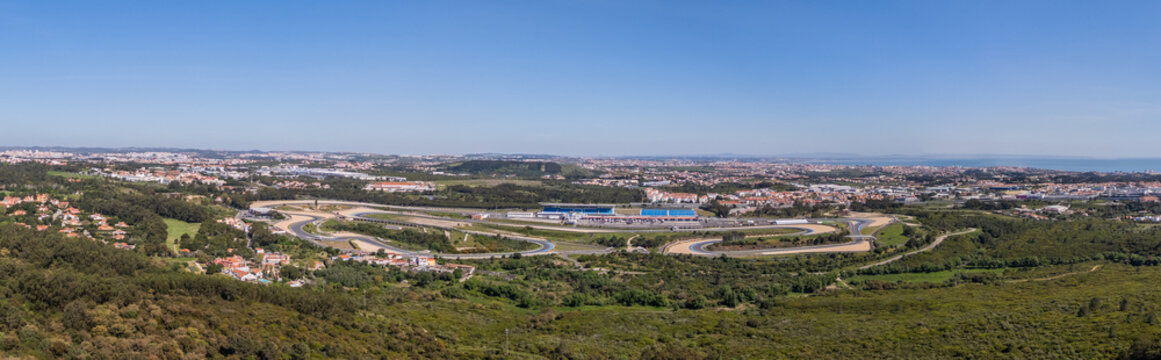 Alcabideche, Portugal - 03 April 2026: Aerial view of Autodromo Fernanda Pires da Silva racing circuit with its winding track, grandstands, and surrounding green hills under a clear blue sky.
