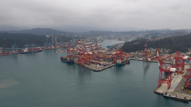 Keelung City, Taiwan - 20 February 2026: Aerial view of Inner Harbor of Keelung with red container cranes, cargo ships, and surrounding green hills under a cloudy sky.