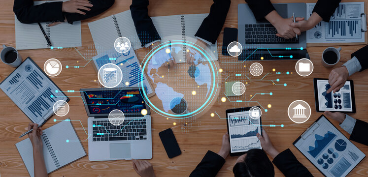A dynamic business meeting scene showcasing professionals collaborating over digital devices, with global data visualizations and analytical reports on a wooden table. Trope