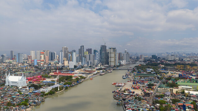 Manila, Philippines - 01 March 2026: Aerial view of Manila Multipurpose Terminal with shipping containers along the Pasig River and the city skyline under a cloudy sky.