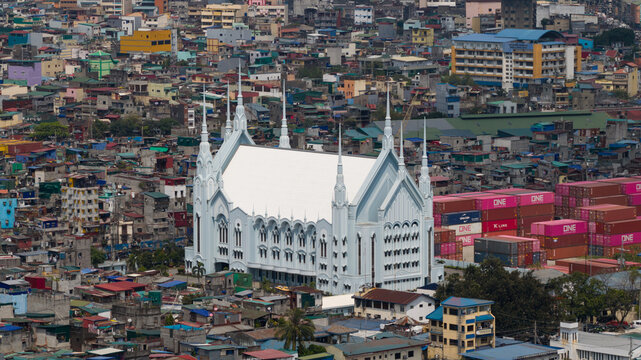 Manila, Philippines - 01 March 2026: Aerial view of a large white church with multiple spires surrounded by dense urban housing and shipping containers at the Manila Multipurpose Terminal.